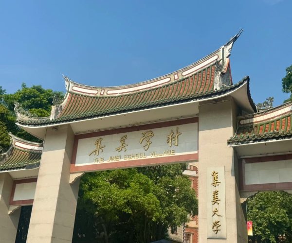 Jimei Educational Village,Xiamen,Chinatravel Entrance gate with traditional curved roof and gold inscription reading 'THE JIMEI SCHOOL VILLAGE' against a blue sky and green trees behind.
