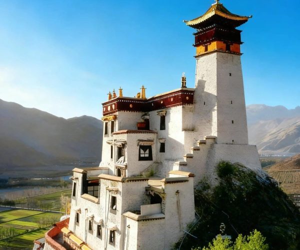 Yumbulakhang Palace,Shannan,China tour Tibetan-style white monastery tower perched on a hillside under a blue sky, with surrounding greenery and distant mountains.