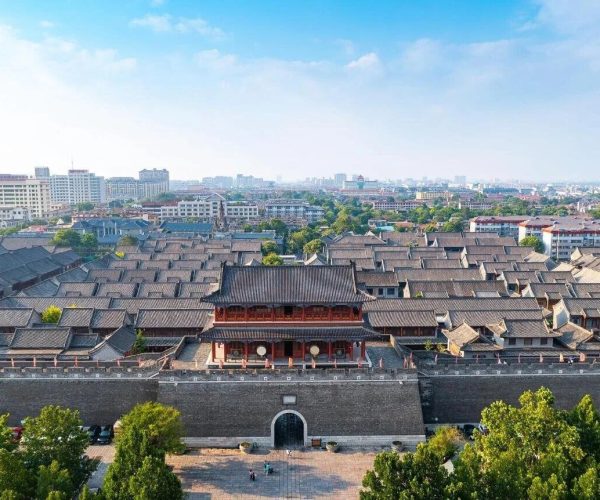 Qingzhou Ancient City,Weifang,China tour Aerial view of a historic walled city with gray-tiled rooftops, a prominent red gatehouse, and a deep stone wall surrounding dense traditional buildings with a modern cityscape in the distance.