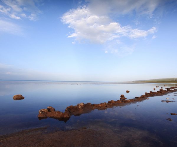 Qinghai Lake ,Xining,Chinatrip Calm shallow lake with a line of brown rocks extending into the water under a clear blue sky.
