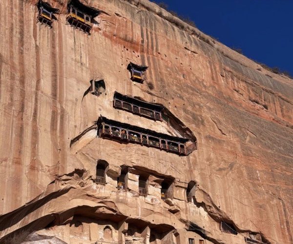 Mati Temple Grottoes,Zhangye,China tour Ancient cliffside temple complex carved into a sandstone cliff with multi-tier wooden balconies under a blue sky