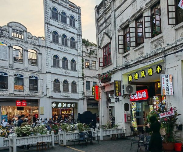 Qilou Old Street,Haikou,Chinatravel Outdoor plaza lined with white colonial buildings, people dining at tables along a low white fence with flowers, bright storefront signs in Chinese nearby.