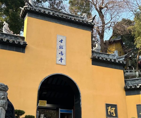 Jiming Temple,Nanjing,China tour Yellow temple gate with a curved tiled roof and blue Chinese character plaque above the arched entrance; visitors walk inside on a sunny day.