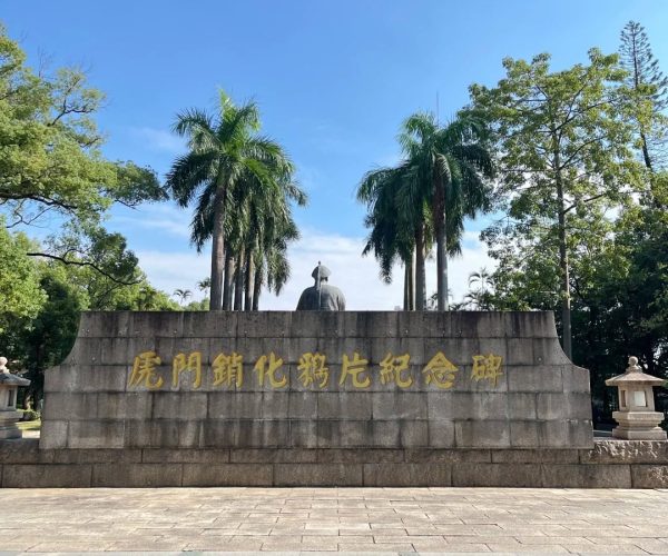 Opium War Museum,Dongguan,Chinatravel Stone monument with gold Chinese inscription, statue behind, palm trees and blue sky above.