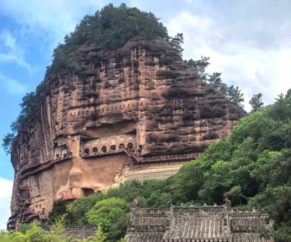 Maijishan Grottoes,Tianshui,China tour Massive rocky mountain carved with cliff-side temple niches and a traditional Chinese gate at its base, set among trees.