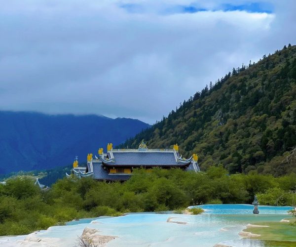 Huanglong Temple,Westren Sichuan,Chinatravel Tiered traditional Chinese temple roof visible among trees, with turquoise terraced pools in the foreground and forested mountains in the distance.