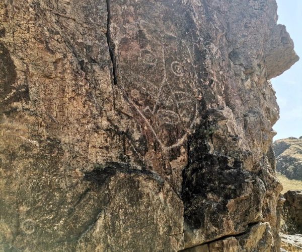 Rocky cliff face with faint ancient petroglyphs carved into stone, including circular spirals and geometric shapes