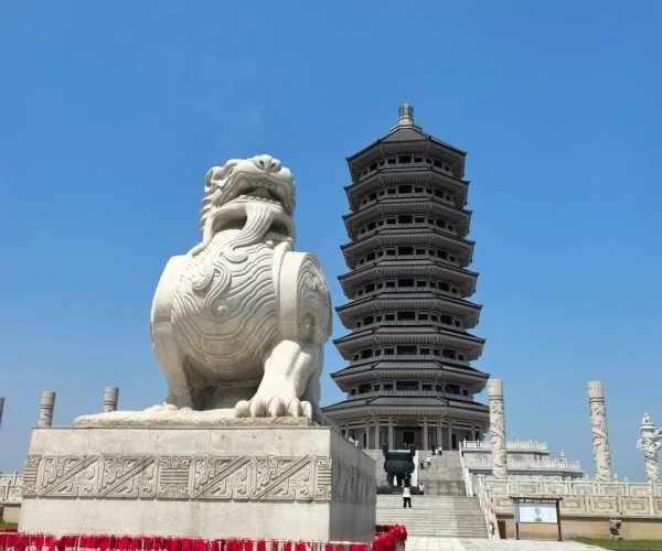 Heixiazi Island Tourist Area,Jiamusi,Chinatravel Large white stone guardian lion statue in front of a multi-tiered pagoda under a clear blue sky.