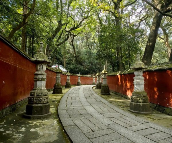 Drum Mountain Scenic Area,Fuzhou,Chinatravel Curved stone path flanked by ornate stone lanterns along a red wall, in a forested temple garden.