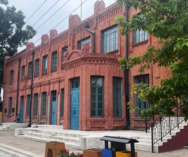 Russia Street,Qiqihar,Chinatravel Red brick historic building with blue doors and windows, decorative brickwork, and a staircase on the right surrounded by greenery.