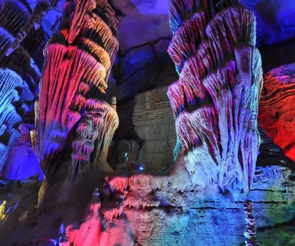 Dragon Palace Scenic Area,Anshun,Chinatravel Colorfully lit cave interior with towering ribbed stalagmites bathed in blue, red, and purple light edges the scene.