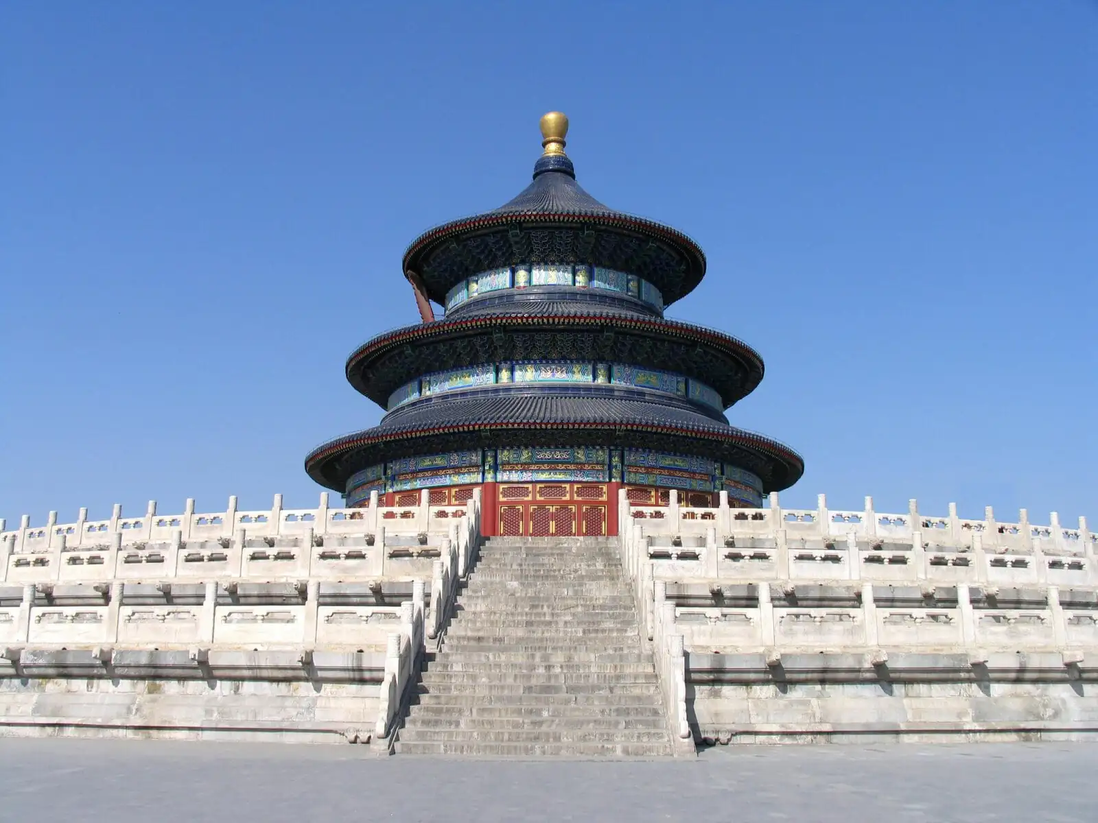 Temple of Heaven, Beijing, Chinatrip, Circular, multi-tiered Chinese temple with blue-green ceramic tiles and gold accents, perched on a stone stairway with a white railing under a clear blue sky.