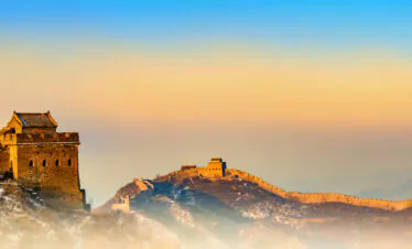 Great Wall of China winding over rocky hills at golden hour, with snow-dusted rocks and a blue-orange sky