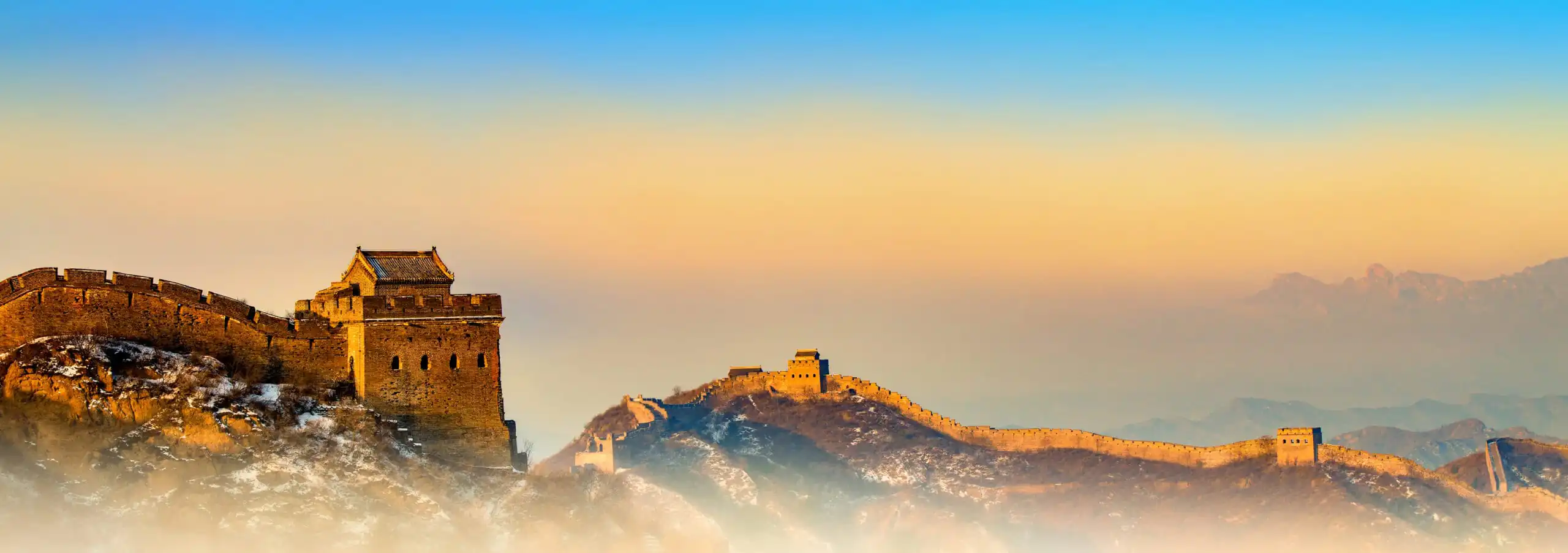 the great wall, Beijing, chinatravel, Great Wall of China winding over rocky hills at golden hour, with snow-dusted rocks and a blue-orange sky