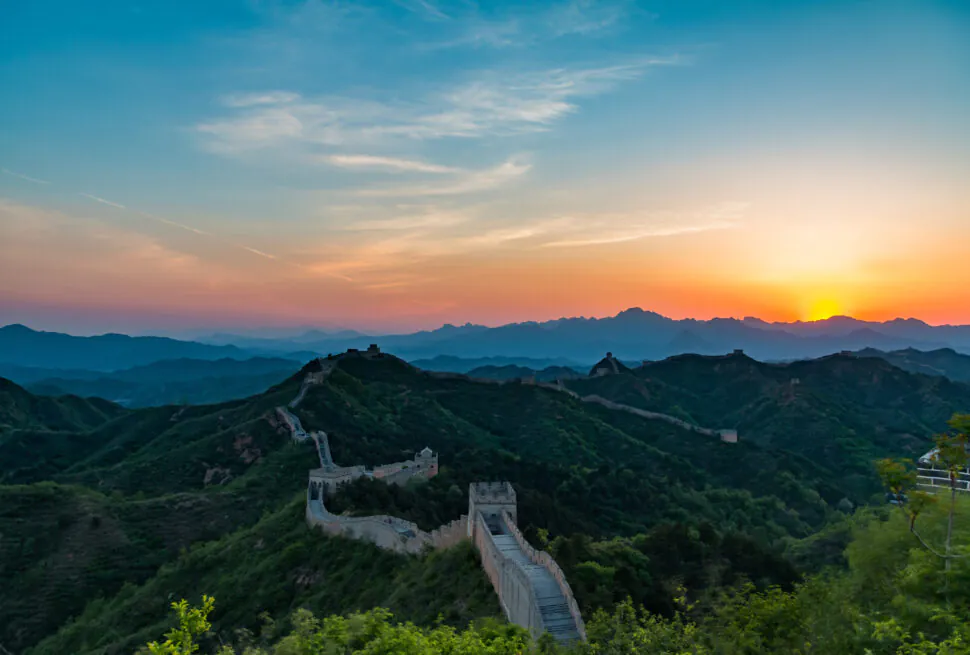 Sunset lights up the Great Wall winding over green hills and watchtowers at dusk.
