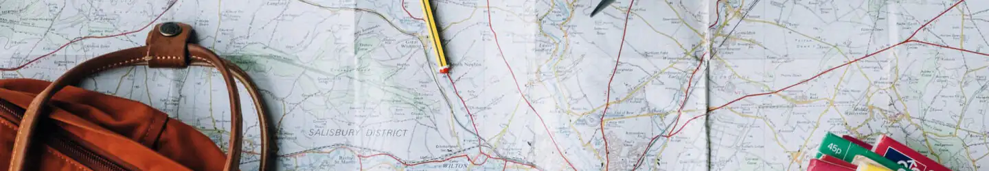 Map spread on a table with a brown leather backpack, pencils, and a ruler nearby.
