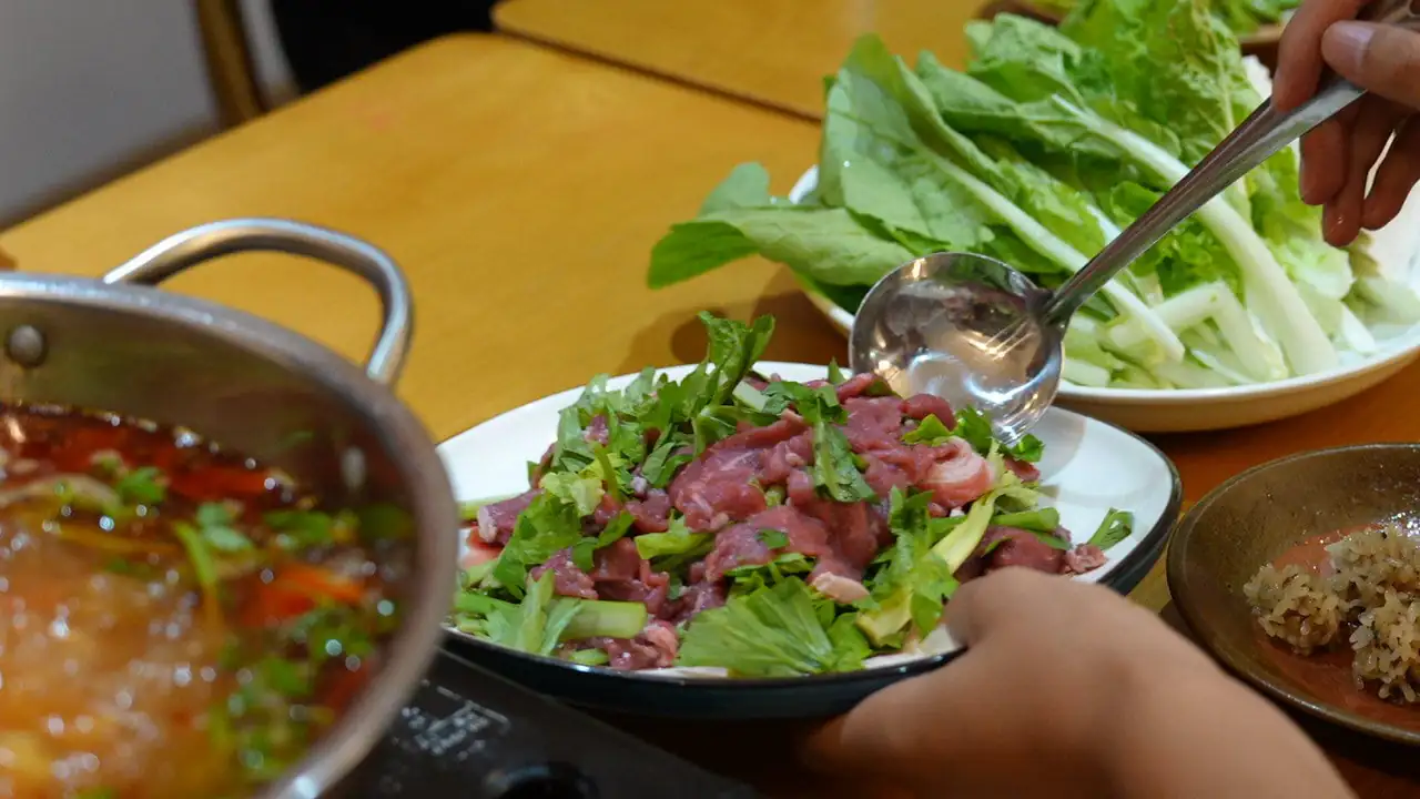 guizhou food, china, china tour, Plate of thin beef and fresh greens (cilantro and lettuce) ready for hot pot, with a hand using a ladle nearby.