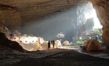 14-Day China Cultural Odyssey: From Iconic Landmarks to Hidden Gems, china, china tour, Cave interior with a row of beige tents and camping chairs, sunlight at the cave entrance, several people walking together.