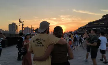 xi'an, china, china tour, Couple embraces on a historic city wall at sunset, with a crowd and modern high-rises in the background.Months tone can vary, but keep to the sense of scene and mood.