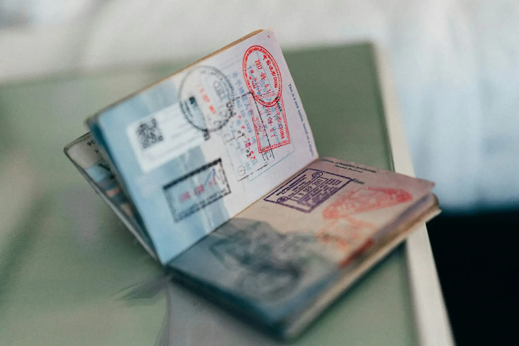 China Travel Guide 2025: Visa, Transportation, Itineraries and More, chinaexplorertour, Close-up of stacked passports with red and blue visa stamps visible on the pages, resting on a surface.