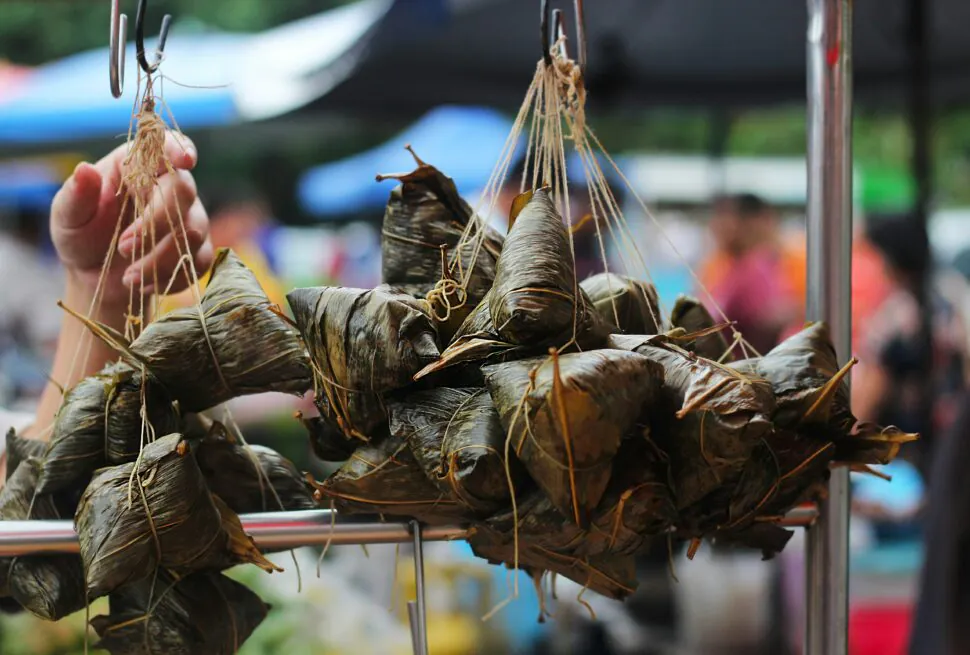 Zongzi, Chinese Festivals: How to Appreciate Food Culture, chinaexplorertour , Hanging bundles of sticky rice dumplings wrapped in bamboo leaves at a street market.