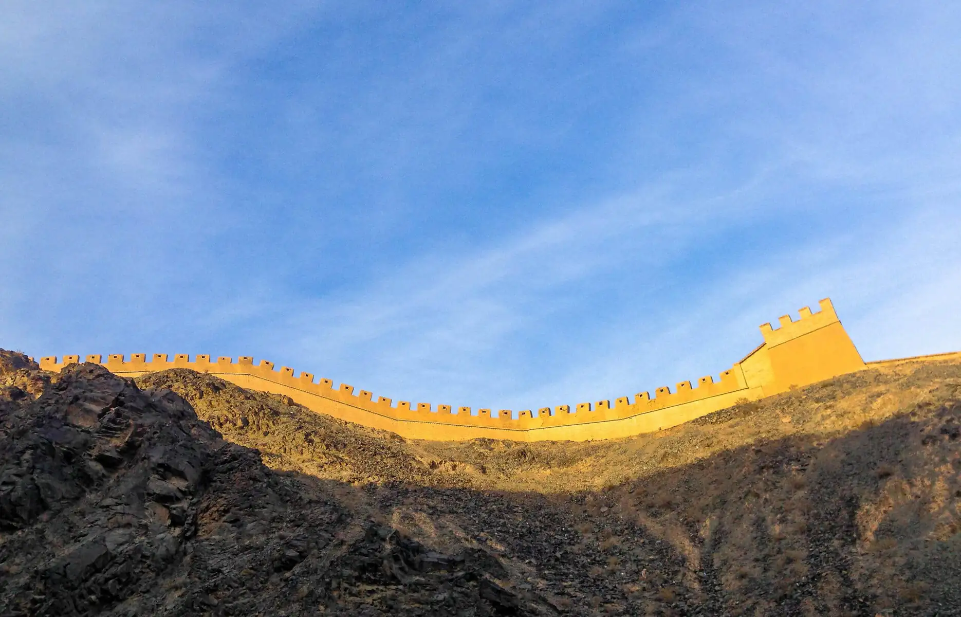 the great wall, Beijing, chinatravel, Curved stone fortress wall with crenellations along a rocky hillside under a clear blue sky