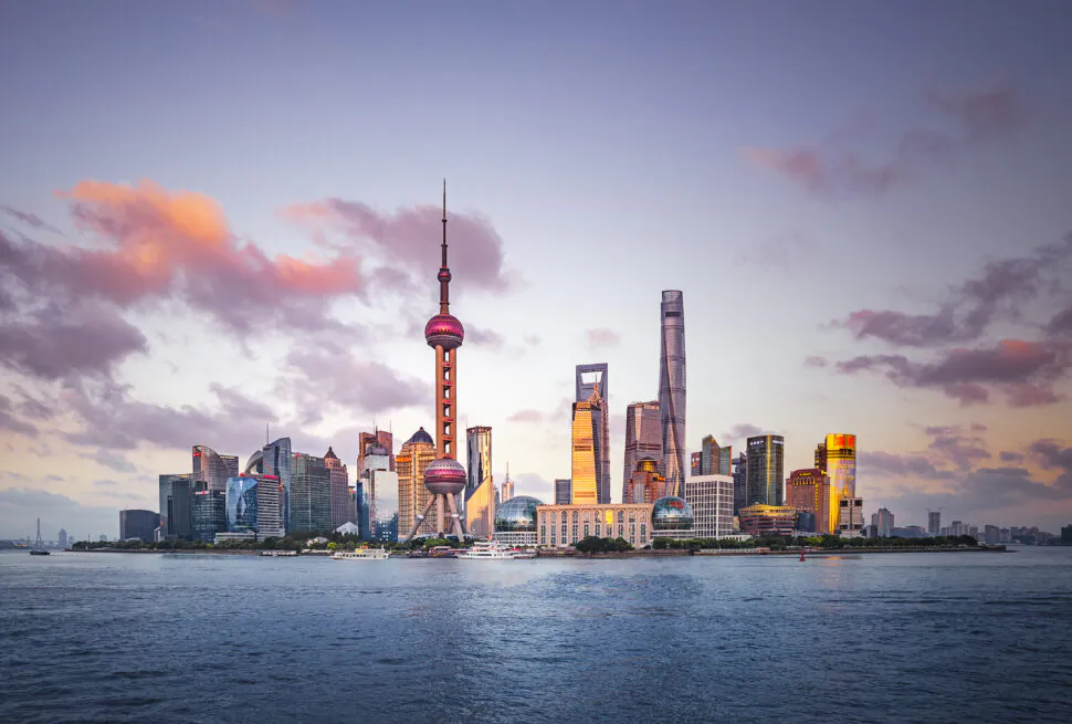 Shanghai Oriental Pearl Tower, china, chinaexplorertour, Skyline of Shanghai at sunset with the Bund along the foreground and tall modern skyscrapers, including the Oriental Pearl Tower, under a pink-orange sky over the water.