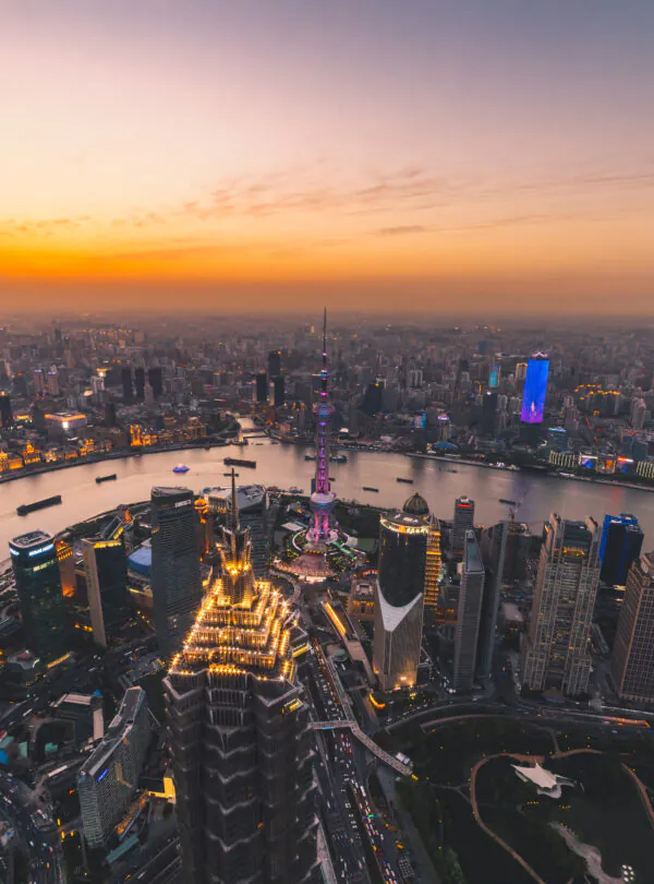 Shanghai, A Guide to Chinese Accommodation: Hotels, Hostels, and More, chinaexplorertour, Aerial view of Shanghai skyline at sunset with the Huangpu River and illuminated skyscrapers, including the Oriental Pearl Tower in the center.