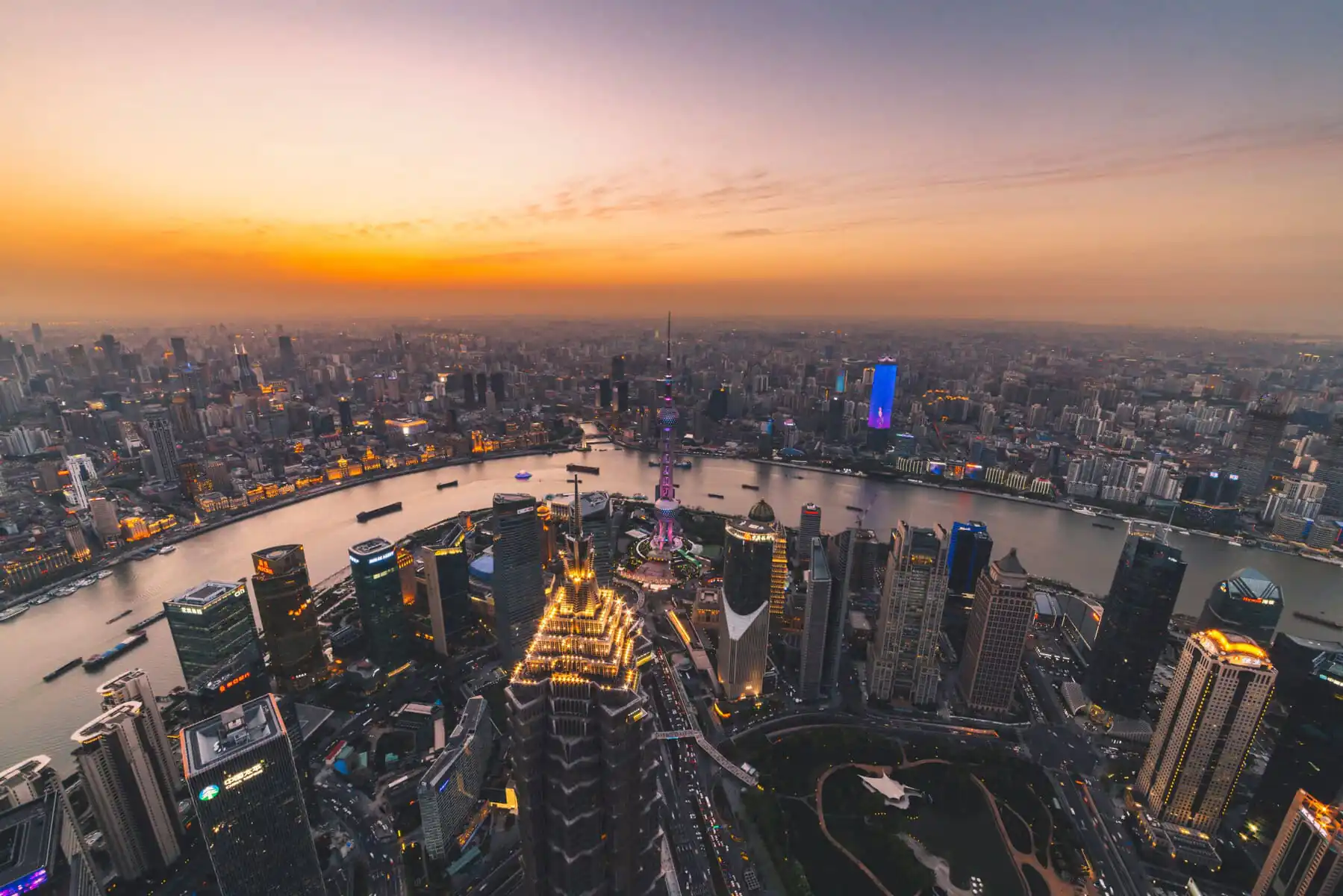 Shanghai, A Guide to Chinese Accommodation: Hotels, Hostels, and More, chinaexplorertour, Aerial view of Shanghai skyline at sunset with the Huangpu River and illuminated skyscrapers, including the Oriental Pearl Tower in the center.