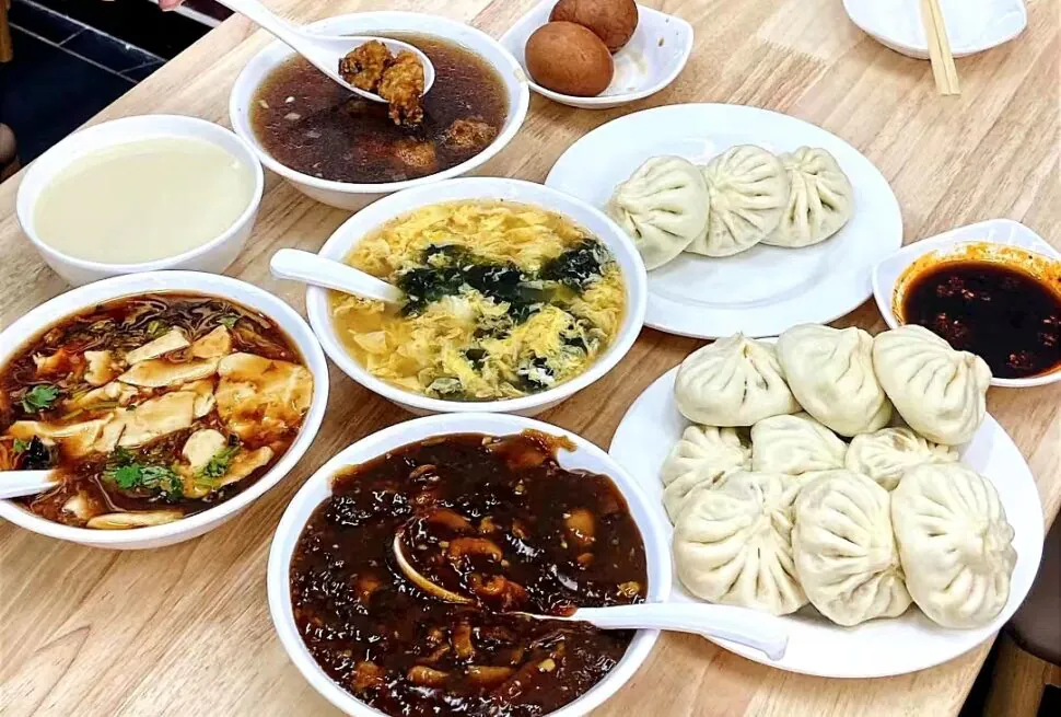 Traditional Chinese Breakfast, china, chinaexplorertour, Steamed dumplings on a white plate with several bowls of soup and sauces on a wooden table.