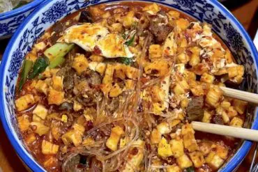 Xi'an Food, Stir Fried Bao Mo, china, chinaexplorertour, Blue patterned bowl of spicy tofu and glass noodle dish with chili oil, minced vegetables and greens; chopsticks rest on the side.