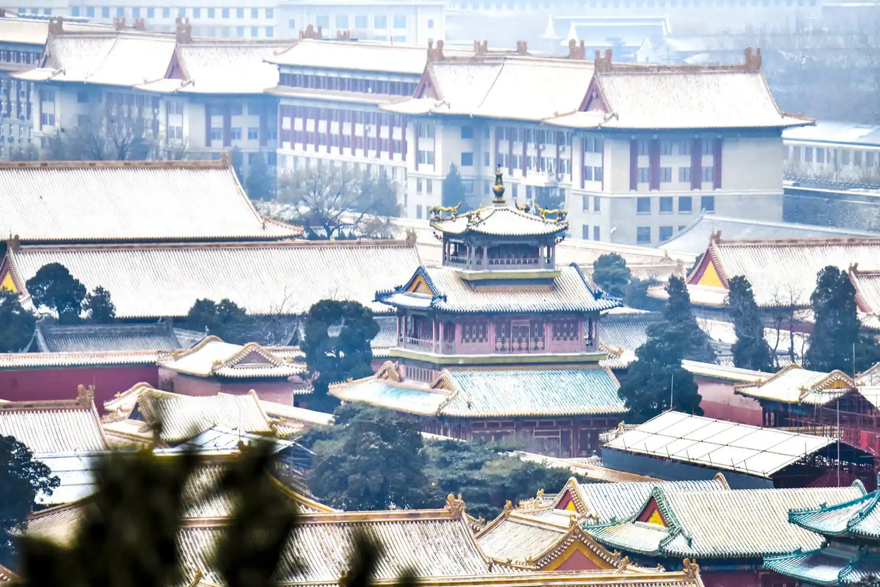 the forbidden city, snow view, beijing, chinatravel, Wide view of a Chinese temple complex with layered, gold-tiled roofs and a central ornate pagoda-like structure in the foreground.