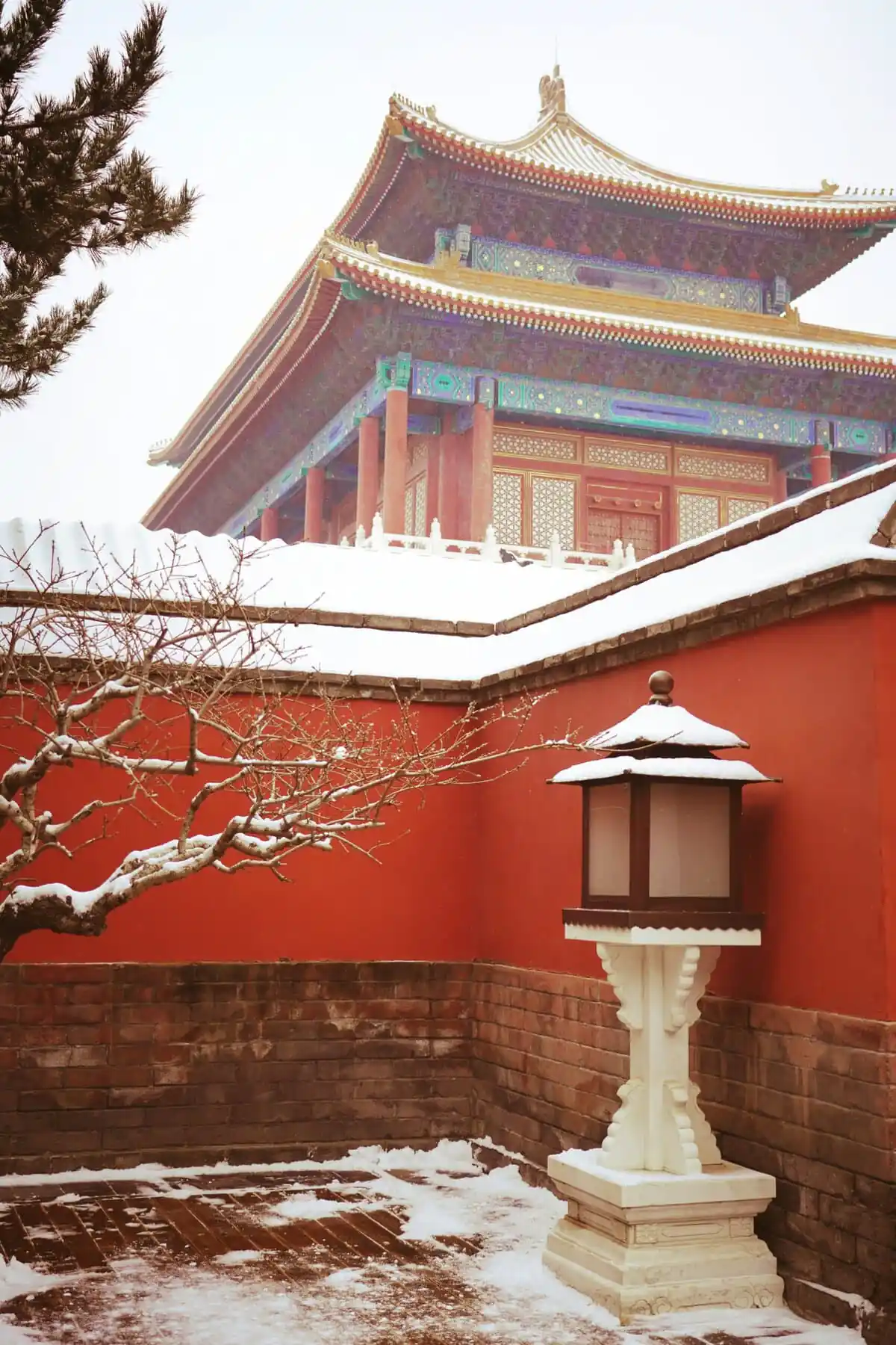 the forbidden city, snow view, beijing, chinatravel, Snow-covered temple courtyard with red walls and ornate multi-tiered roof; foreground white lantern and snow‑capped branches in the foreground.