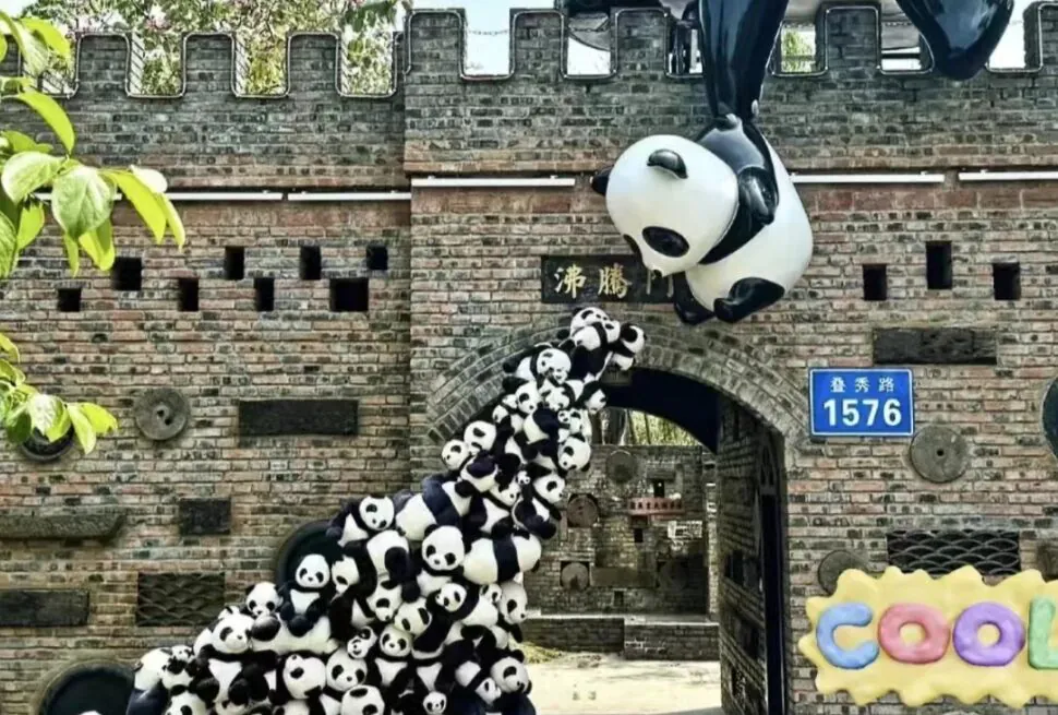 Chengdu Trip, sichuan, china, china tour, Panda sculptures stacked on a brick wall archway as if climbing, with a large floating panda overhead and a blue 1576 sign nearby.