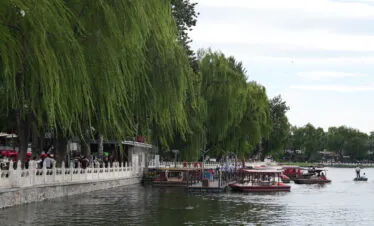 Shichahai, beijing, china, china tour, Riverside promenade with weeping willow trees, a white railing, and people walking by the water with boats docked nearby