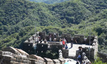 great wall, beijing, china, china tour, Tourists walk along the stone Great Wall walkway with crenellations, overlooking green forested hills.