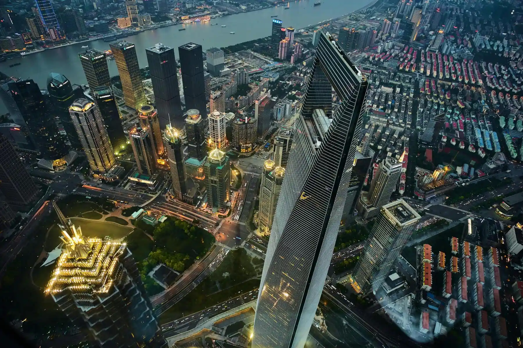 shanghai, china, china tour, Aerial view of Shanghai's skyline with skyscrapers along a river and a distinctive triangular glass tower at center. Avoids