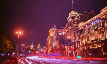 shanghai, china, china tour, Nighttime city street with illuminated historic buildings and neon signs; long exposure light trails from passing cars create red and white streaks.