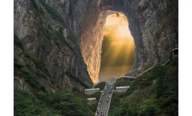 Tianmen Mountain, Zhangjiajie, hunan, china, chinatrip, A long stairway winds up a forested valley toward a massive rock arch with sunlight streaming through the opening.