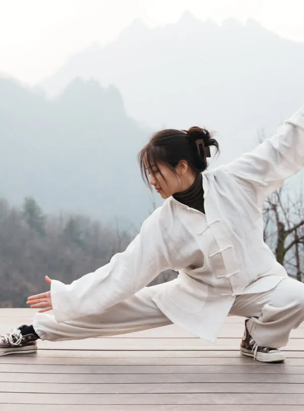 Wudang, shiyan, hubei, china tour, Person in a light beige martial arts outfit performing a low stance on a wooden deck with misty mountains in the background