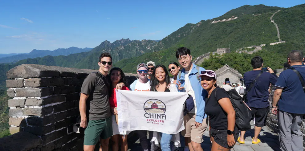 Mutianyu Great Wall, Beijing, Chinatravel, Group of diverse tourists posing with a China Explorer Tour banner on the Great Wall, blue sky and green mountains in the background.
