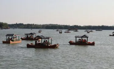 Summer Palace, beijing, china, chinatrip, Multiple wooden boats with canopies carrying groups of people on a calm lake, with a tree-lined shore in the distance under a clear sky.