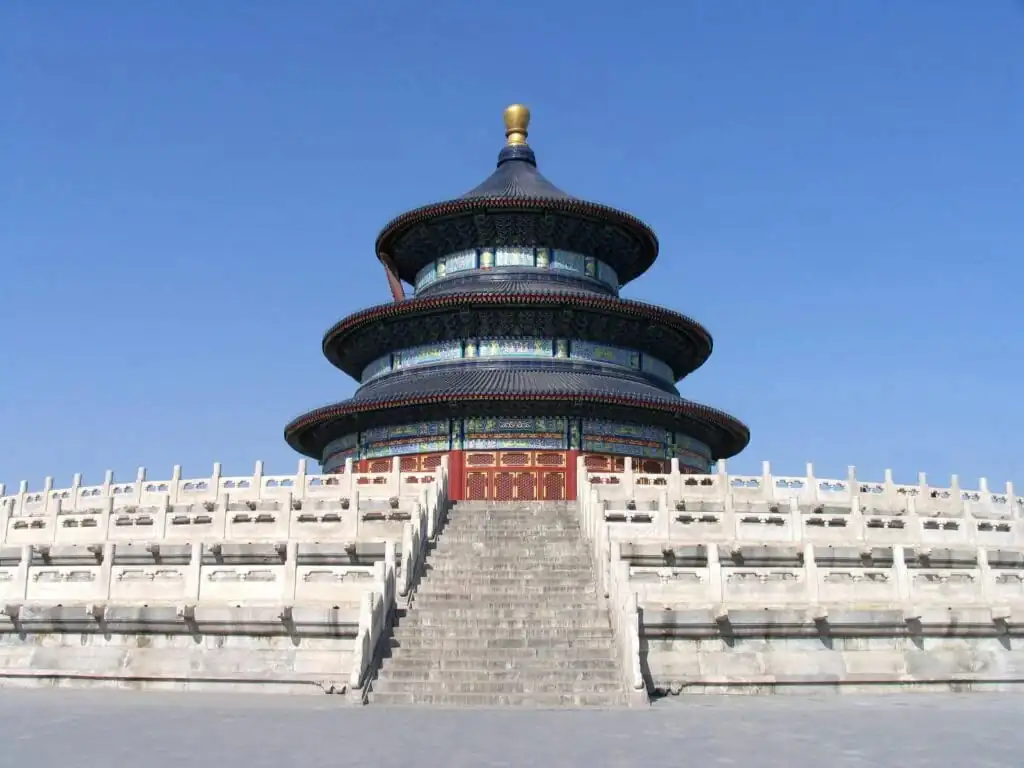 the temple of heaven, beijing, china tour, Three-tiered circular temple with blue-tiled roofs atop a white stone terrace, reached by a long stairway, under a clear blue sky (Temple of Heaven, Beijing)