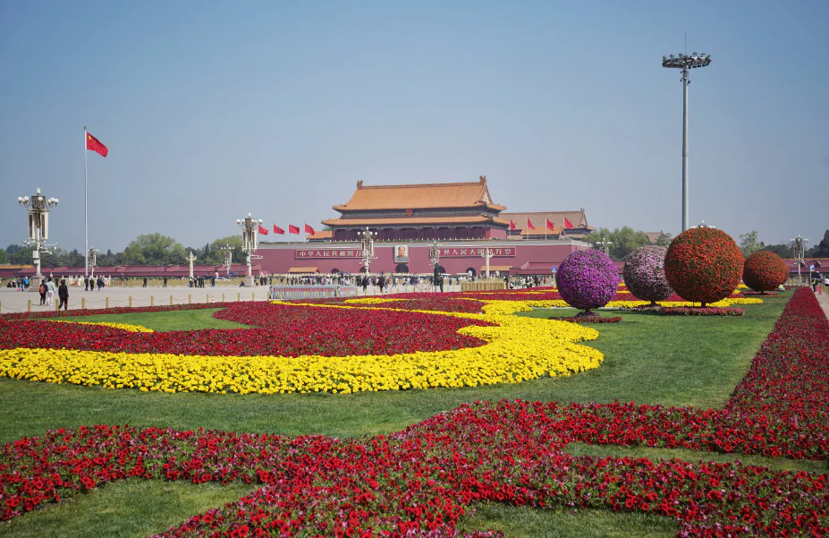 Tiananmen Gate, beijing, china tour, Wide view of Tiananmen Gate with red flags, seen behind colorful flower beds in the foreground: yellow, red, and purple patterns.