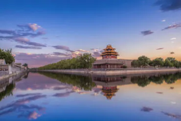 the forbidden city, Discover the Wonders of China with China Explorer Tour, Traditional Chinese pagoda on a stone platform beside a tree-lined waterway at sunset, reflected in calm water.