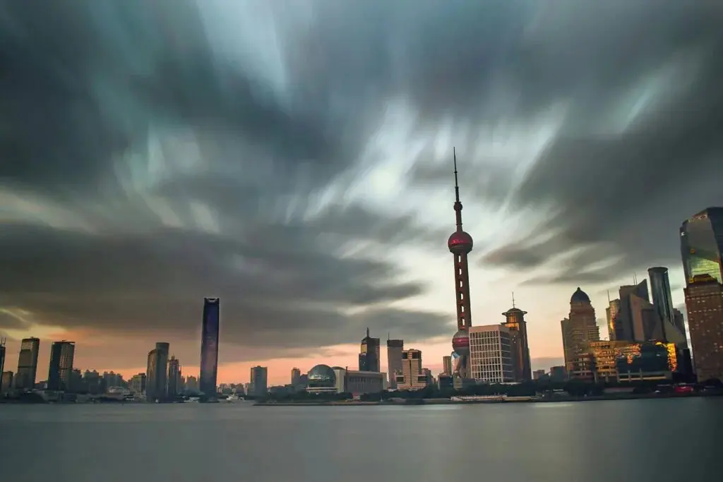 Shanghai City Tours, china tour, Shanghai skyline across the Huangpu River at sunset, with the Oriental Pearl Tower amid tall modern buildings and a cloudy sky