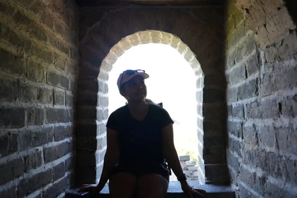 the great wall, Why Indian Travelers Love China Explorer Tour, Person wearing a cap sits on a stone ledge inside a dark brick archway, with bright daylight visible outside behind them (backlit scene).