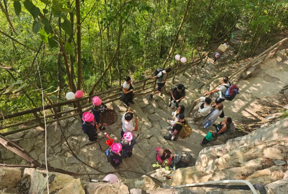 Guizhou: Your Guide to Shuicheng County, china tour, Group of people gathered on a stone outdoor stairway in a forest, some wearing pink hats, with balloons tied to the railing.