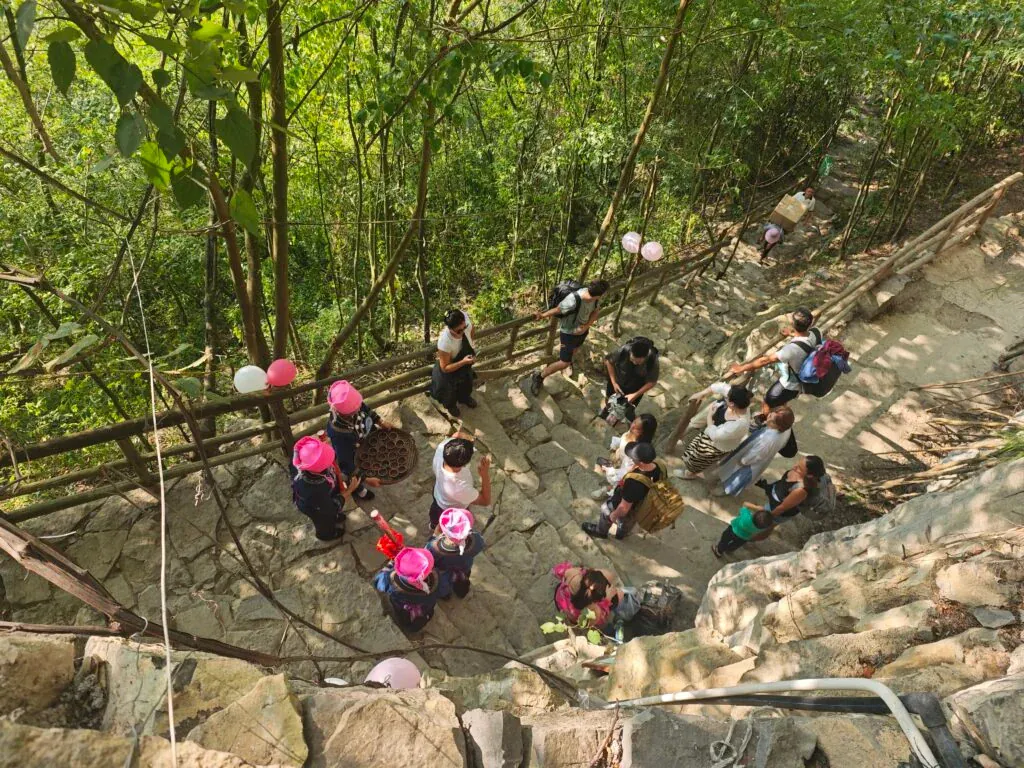 Guizhou: Your Guide to Shuicheng County, china tour, Group of people gathered on a stone outdoor stairway in a forest, some wearing pink hats, with balloons tied to the railing.