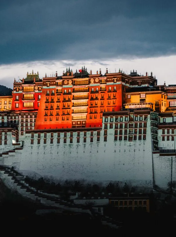 Potala Palace Tibet, china, china tour, Potala Palace perched on terraced hills with warm orange buildings under a dramatic, dark storm sky at dusk.